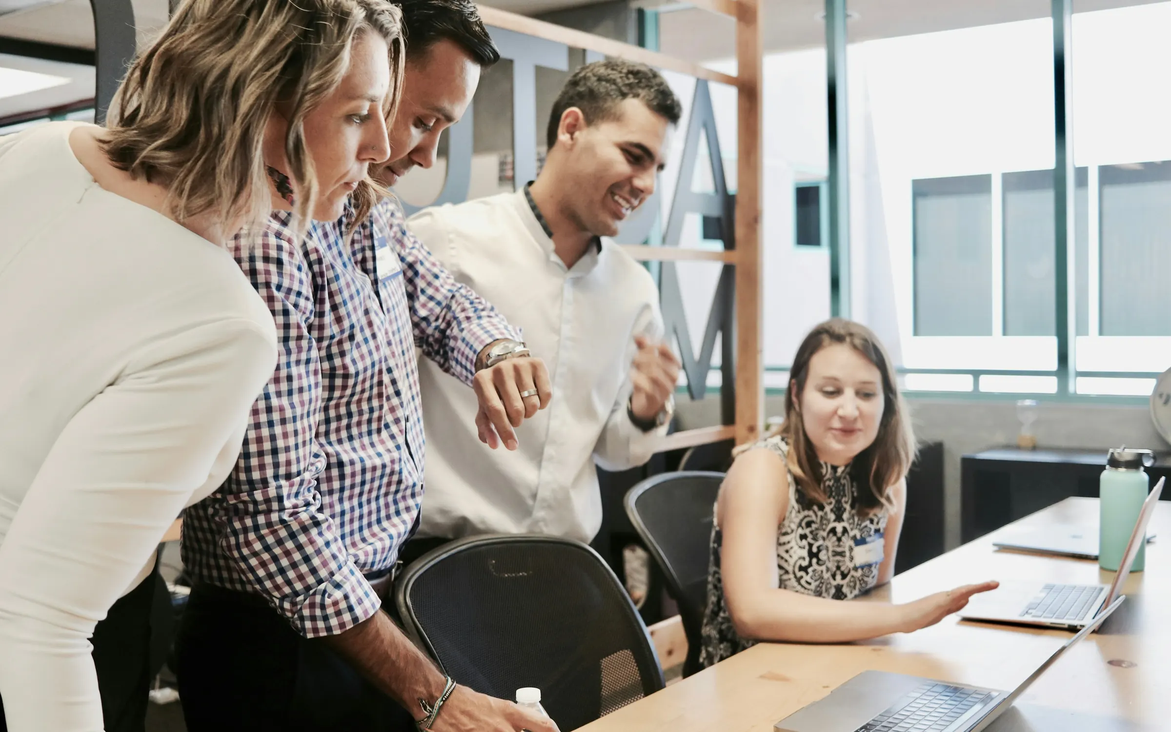 Colleagues gathered around a laptop discussing work in a bright office