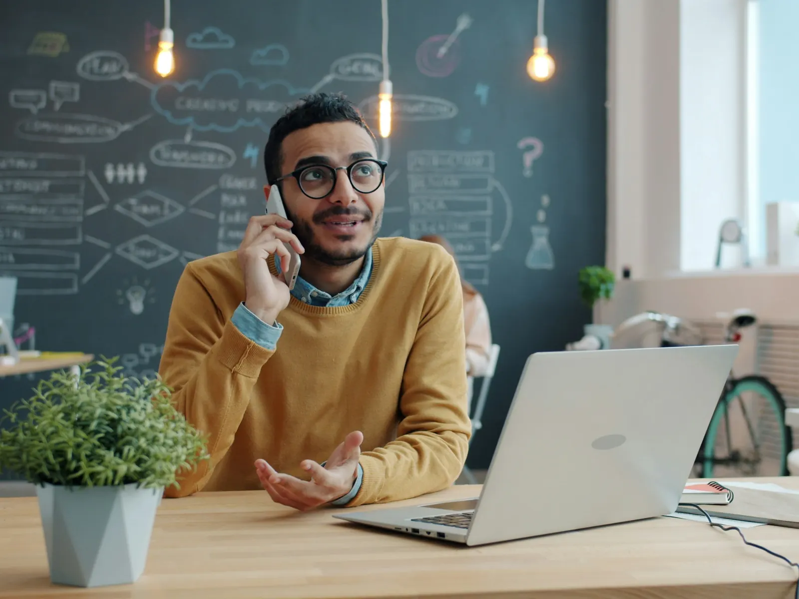Man talking on his phone at a desk with a laptop
