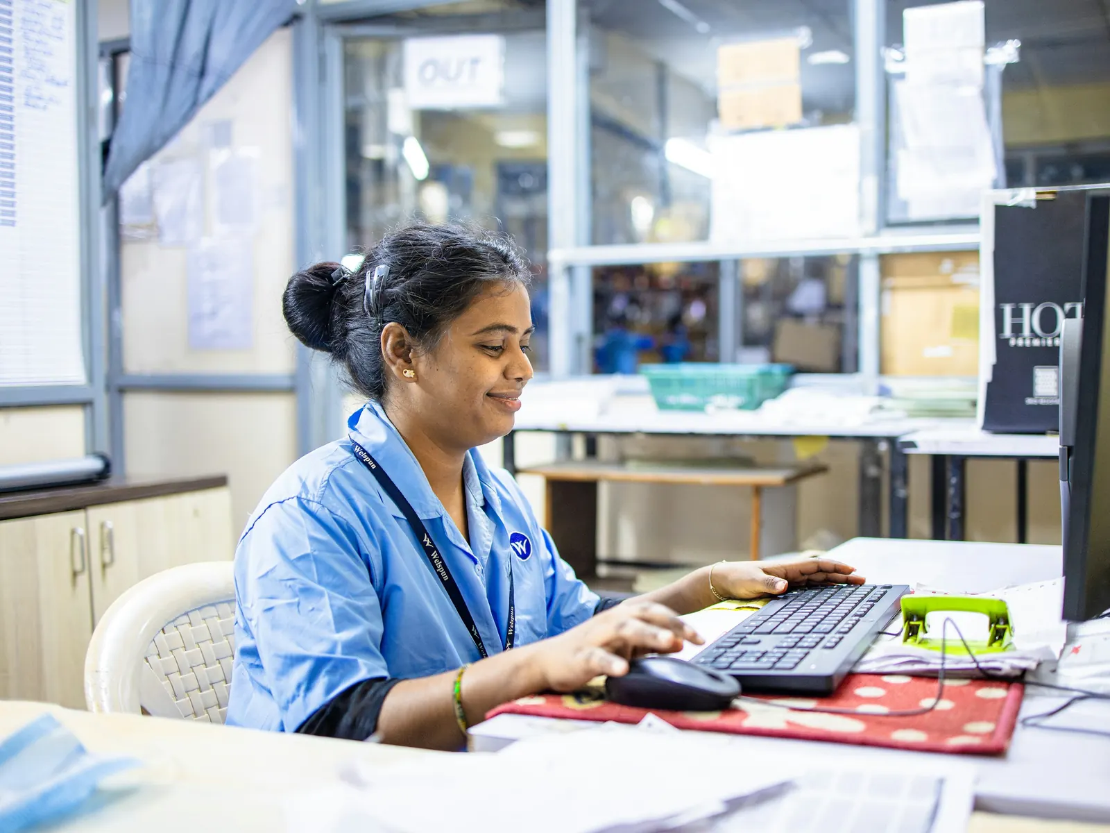Staff member in a blue uniform working through records at a desktop computer