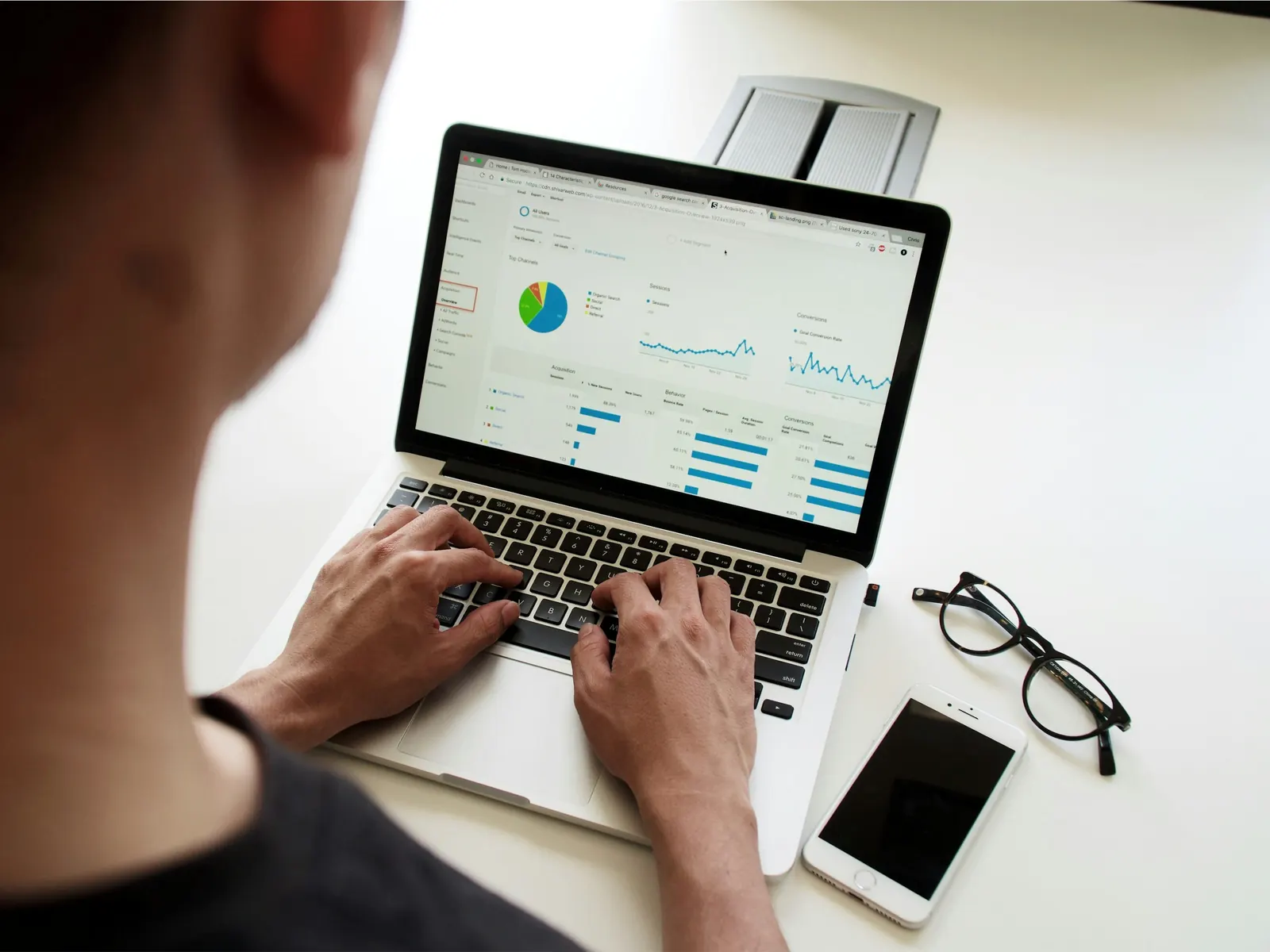 Analyst typing on a laptop showing data charts beside glasses and a phone