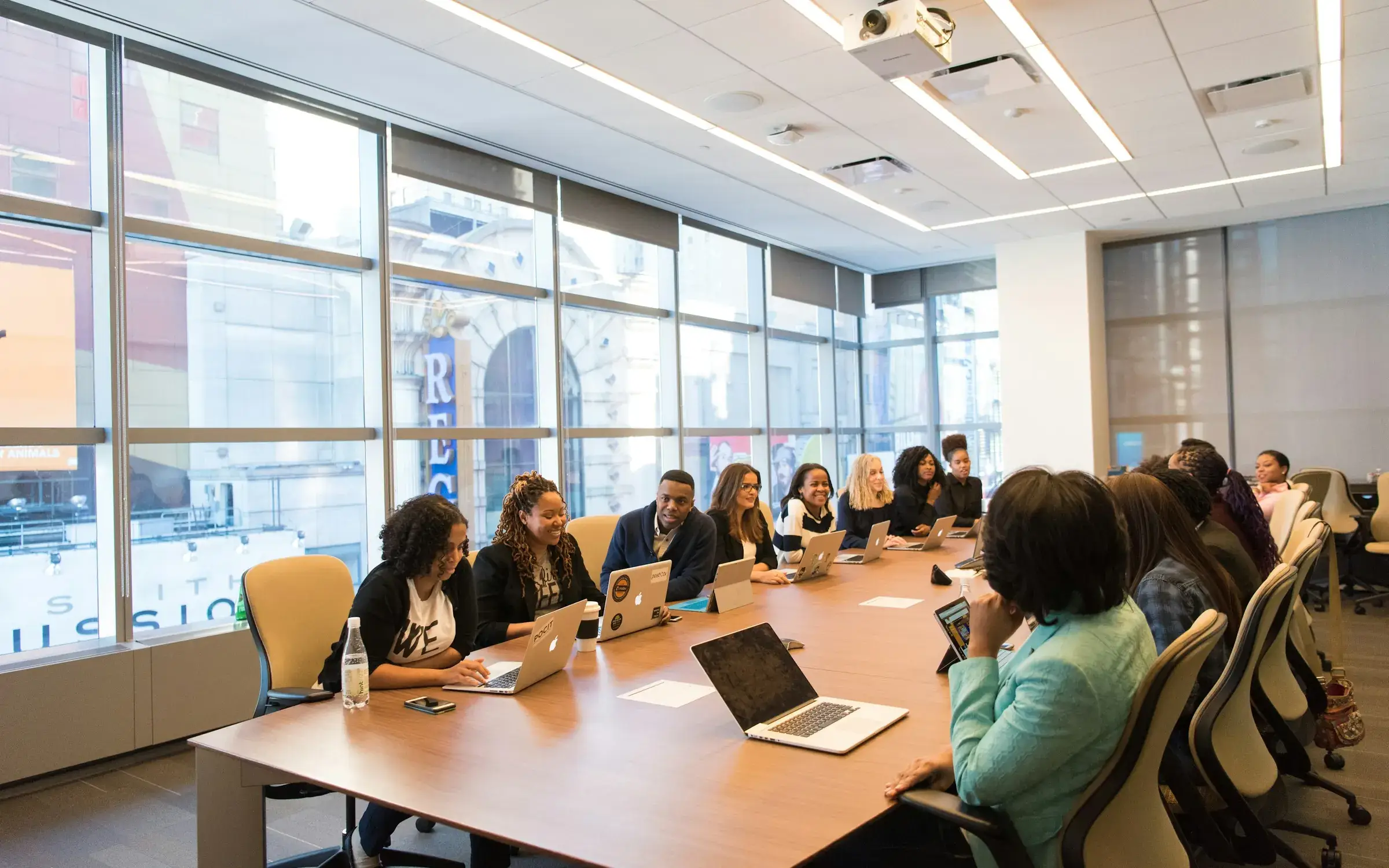 Team working with laptops around a long boardroom table in a sunlit office